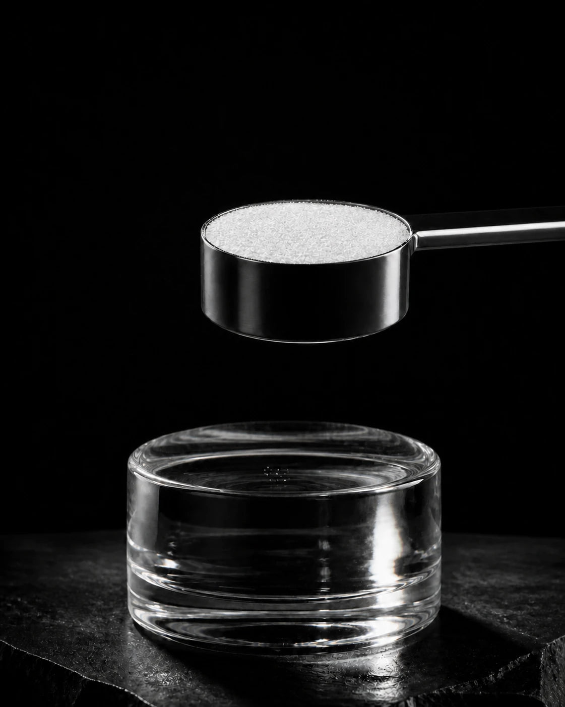 A level black scoop of plain white powder above a clear glass form